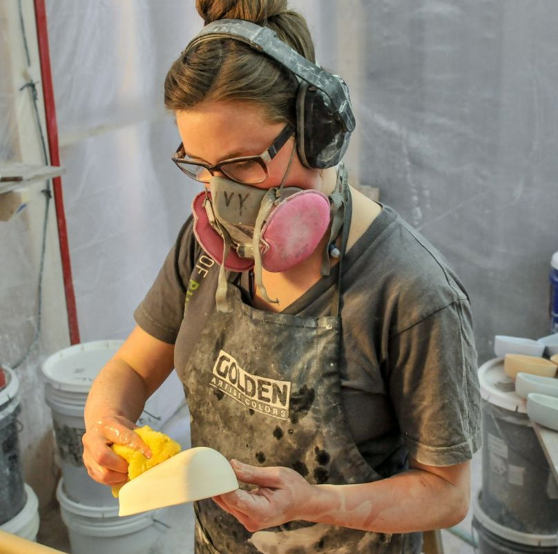 A caster wearing protective gear sponges off a piece